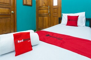 A hotel room with a bed, a red and white bedspread, and a red pillow with the RedDoorz logo.