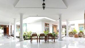 A spacious indoor area with white columns, wooden chairs, and potted plants. - RedDoorz Syariah near Alun Alun Magelang (Magelang)