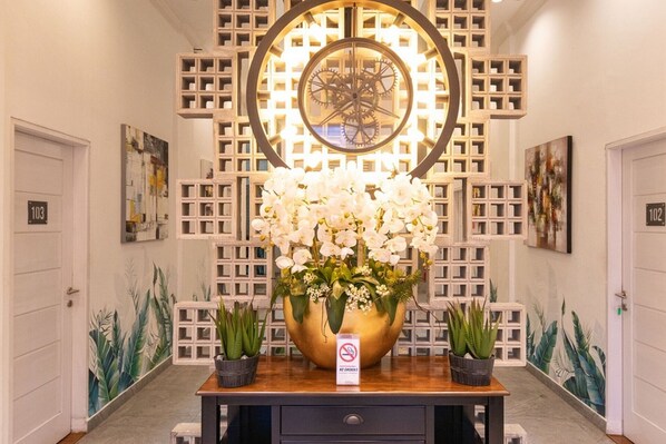 Un hall d’entrée agrémenté d’une grande horloge décorative, d’un arrangement floral et d’un panneau indiquant qu’il est interdit de fumer.