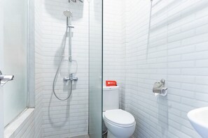 Un baño con paredes de azulejos blancos, cabina de ducha de cristal, inodoro y lavabo.