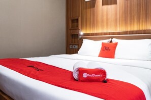 Une chambre d’hôtel avec un lit soigneusement fait, une tête de lit en bois et une couverture rouge ornée du logo RedDoorz.