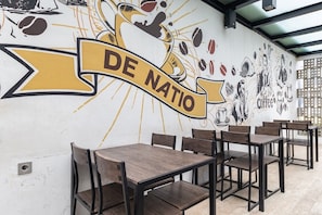 Interior de una cafetería con un mural de arte relacionado con el café y el texto "DE NATIO".