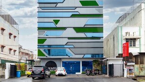 A modern building with a geometric facade, a blue entrance, and a parking area with cars and motorcycles. - RedDoorz Premium near Centre Point Mall Medan (Medan)