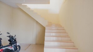 A staircase with white steps leading upwards, a ceiling light fixture, and a parked motorcycle in the foreground. - RedDoorz near RS Imanuel Lampung (Bandar Lampung)