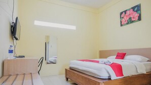 A hotel room with a wooden bed, a desk with a chair, a flat-screen TV, and a painting of flowers on the wall. - RedDoorz near RS Imanuel Lampung (Bandar Lampung)