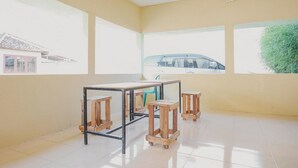 A room with a large window, a table with stools, and a view of a car and greenery outside. - RedDoorz near RS Imanuel Lampung (Bandar Lampung)