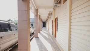 A corridor with a tiled floor, a parked car, and a building with closed shutters. - RedDoorz near RS Imanuel Lampung (Bandar Lampung)