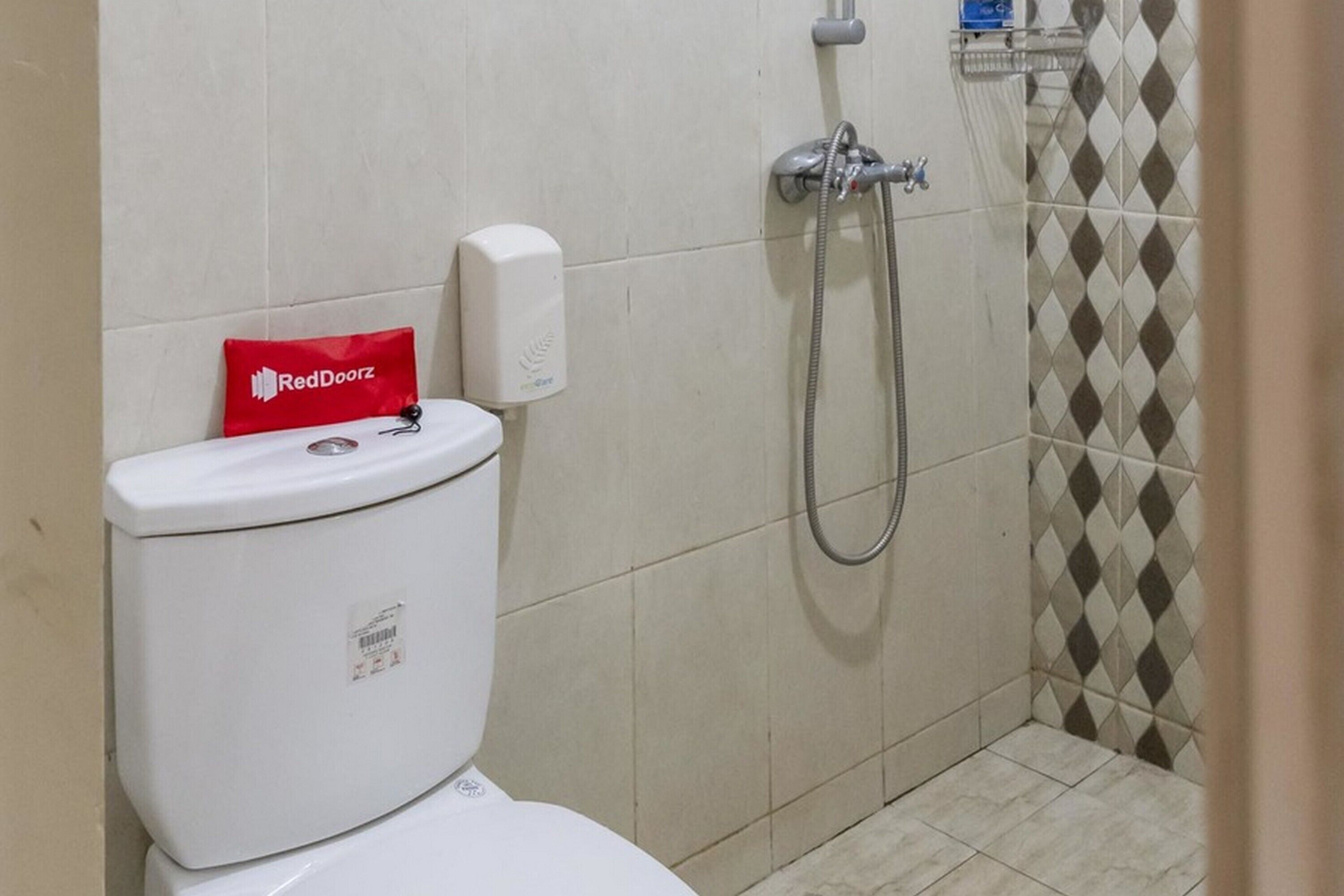 A bathroom with a toilet, a RedDoorz hand sanitizer dispenser, and a shower with a hose.