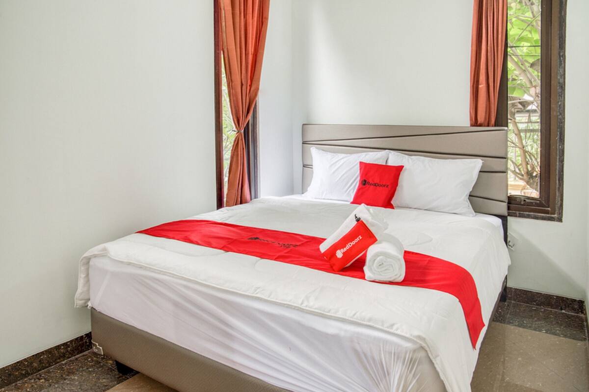 Una cama bien hecha con ropa de cama blanca y roja, una almohada roja y una toalla con un logotipo.