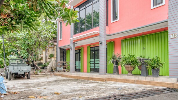 Ein modernes Gebäude mit rosa Fassade, grünen Fensterläden und der Hausnummer 38.