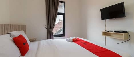 A hotel room with a bed, a TV mounted on the wall, and a window with curtains.