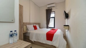 Una habitación de hotel con una cama, un escritorio con botellas de agua, aire acondicionado y un televisor montado en la pared.