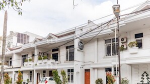 Ein weißes Mehrstöckiges Hotel mit Balkonen, Pflanzkübeln und einem geparkten Auto davor.