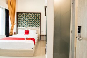 Una habitación de hotel con cama, mesita de noche, televisor montado en la pared y una puerta con picaporte.