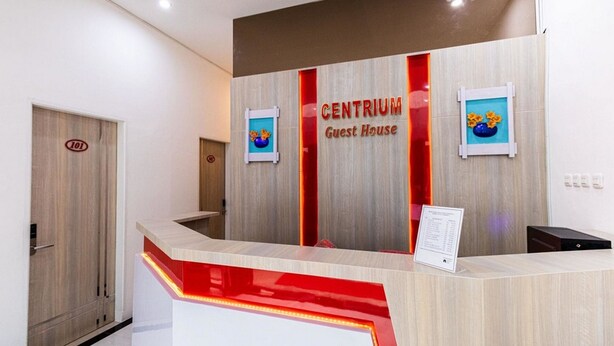 A hotel reception desk with a wooden finish and a red accent. There is a sign above the desk that reads "CENTRIUM Guest House." - RedDoorz Plus @ Centrium Katamso Medan (Medan)