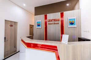 A hotel reception desk with a wooden finish and a red accent. There is a sign above the desk that reads "CENTRIUM Guest House." - RedDoorz Plus @ Centrium Katamso Medan (Medan)