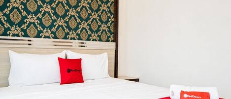 A hotel room with a bed, white bedding, a red blanket, and a red pillow.