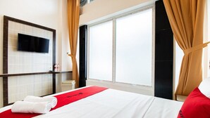 A hotel room with a bed, a TV mounted on the wall, a window with curtains, and a red bed runner. - RedDoorz Plus @ Centrium Katamso Medan (Medan)