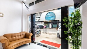 A lobby with a sofa, a red carpet, a glass door leading outside, and a potted plant. - RedDoorz Plus @ Centrium Katamso Medan (Medan)