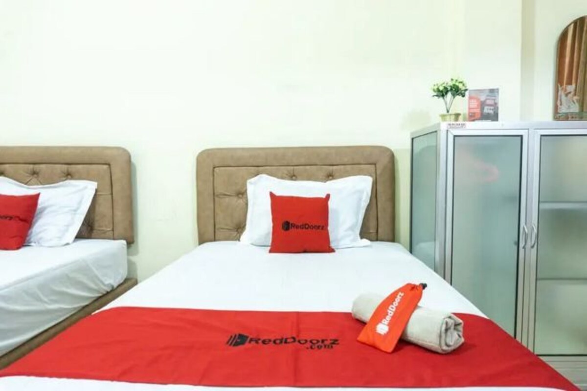 A hotel room with two beds, each with a red and white bedspread, and a RedDoorz logo on the beds.