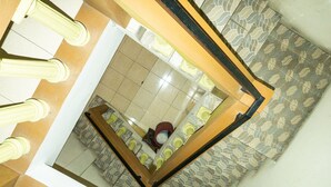 Een hoog hoekig uitzicht op een hotelinterieur met een centrale trap, vloertegels met een patroon en een spiegel die een deel van de kamer weerspiegelt.