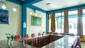 Un salón de conferencias con una mesa de vidrio, sillas rojas, un cuadro y una ventana con cortinas.