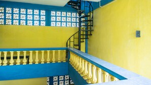 Una escalera con barandilla y balaustrada en azul, que lleva a un rellano con pared de diseño y una ventana con celosía decorativa.