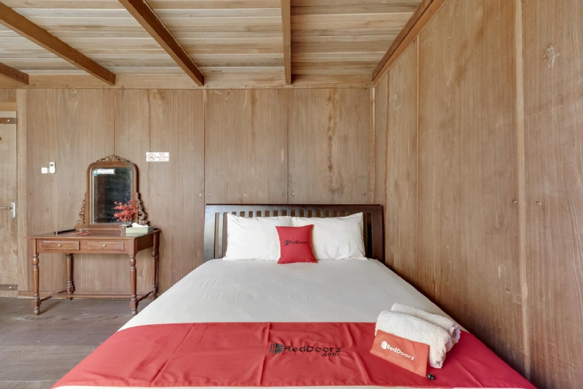 A wooden-paneled room with a bed, a wooden desk, and a mirror.
