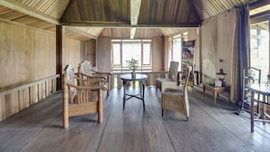 A wooden interior with a high ceiling, wooden flooring, and a central round table surrounded by chairs. - RedDoorz @ Omah Kayu Homestay (Sewon)
