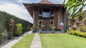 A wooden house with a tiled roof, a concrete pathway, and a well-maintained lawn. - RedDoorz @ Omah Kayu Homestay (Sewon)