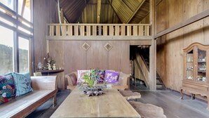A rustic wooden interior with a high ceiling, a wooden bench, a sofa with colorful cushions, and a glass-top table with decorative items. - RedDoorz @ Omah Kayu Homestay (Sewon)