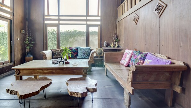 A spacious room with a large wooden table, a wooden bench, and a sofa with colorful cushions. - RedDoorz @ Omah Kayu Homestay (Sewon)