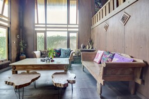 A spacious room with a large wooden table, a wooden bench, and a sofa with colorful cushions. - RedDoorz @ Omah Kayu Homestay (Sewon)