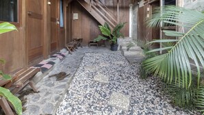 A wooden building with a stone-paved courtyard, wooden benches, and potted plants. - RedDoorz @ Omah Kayu Homestay (Sewon)