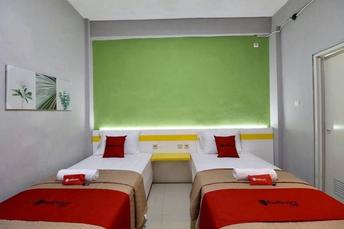 Ein Hotelzimmer mit zwei Betten, einer grünen Akzentwand und einem kleinen Tisch dazwischen.