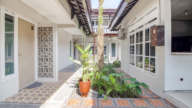 A corridor with tiled flooring, a potted plant, and a door with a decorative grille. - RedDoorz near Malioboro Tugu Station Jogja 2 (Yogyakarta)