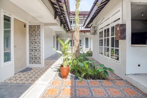A corridor with tiled flooring, a potted plant, and a door with a decorative grille. - RedDoorz near Malioboro Tugu Station Jogja 2 (Yogyakarta)