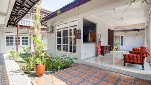 A spacious indoor area with a tiled floor, potted plants, and a red upholstered chair. - RedDoorz near Malioboro Tugu Station Jogja 2 (Yogyakarta)