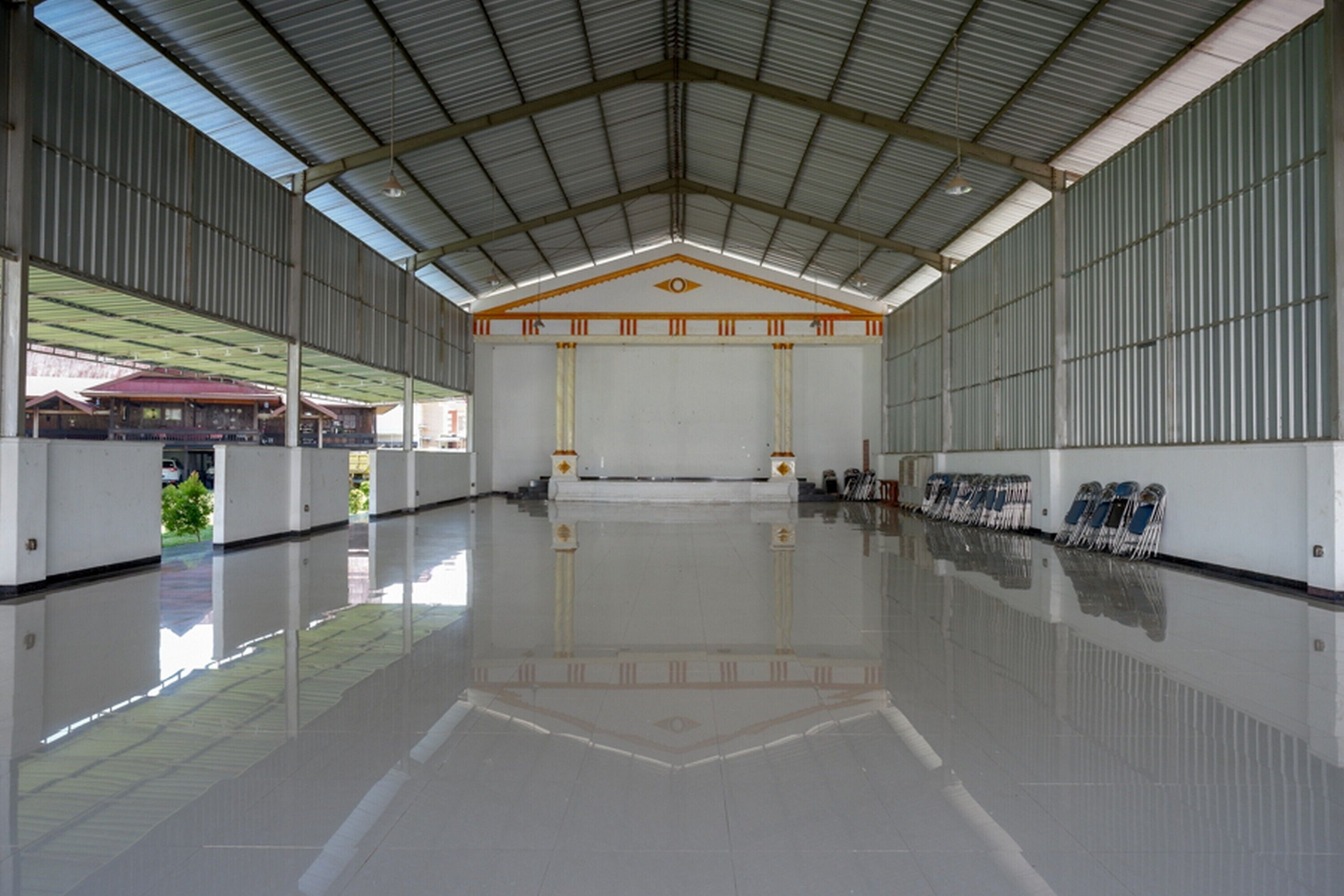 A large, empty indoor space with a high ceiling, reflective floor, and rows of chairs along the walls.