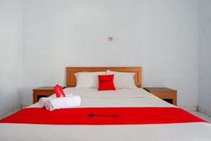 A neatly made bed with a red blanket and pillows, a white towel, and a red tag on the side. - RedDoorz @ Hotel Horas Palopo (Palopo)