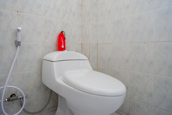 Inodoro blanco con una herramienta de limpieza roja adherida al tanque, una tubería blanca y una pared de azulejos.