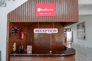 A reception area with a RedDoorz sign, a reception desk, a fire extinguisher, and a bulletin board. - RedDoorz @ Hotel Horas Palopo (Palopo)