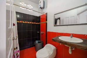 Une salle de bain avec des toilettes blanches, un lavabo et un espace douche aux carreaux noirs et rouges.