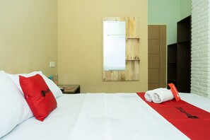 A hotel room with a bed, a red pillow, a white towel, and a red towel on the bed.