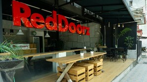 Een buiten eetgedeelte met een houten tafel en stoelen, een RedDoorz bord en potplanten.