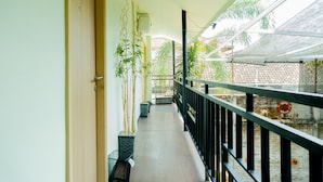 Een gang met een houten deur, planten in potten, een balkon met een hekwerk en uitzicht op een tuin.