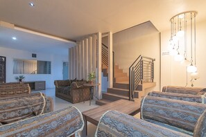 A modern living room with patterned sofas, a wooden coffee table, a staircase, and a hanging light fixture.