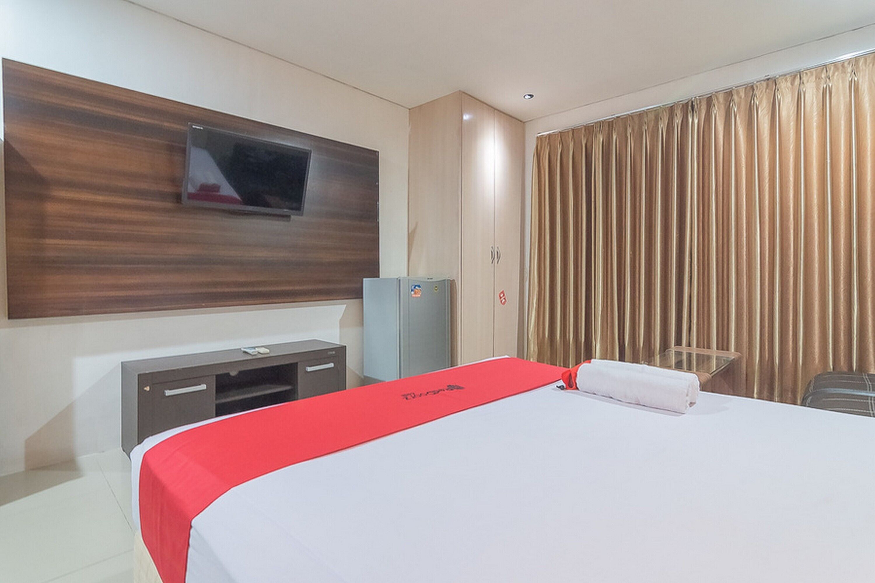 Een hotelkamer met een bed, een aan de muur bevestigde televisie, een minibar en een gordijn.