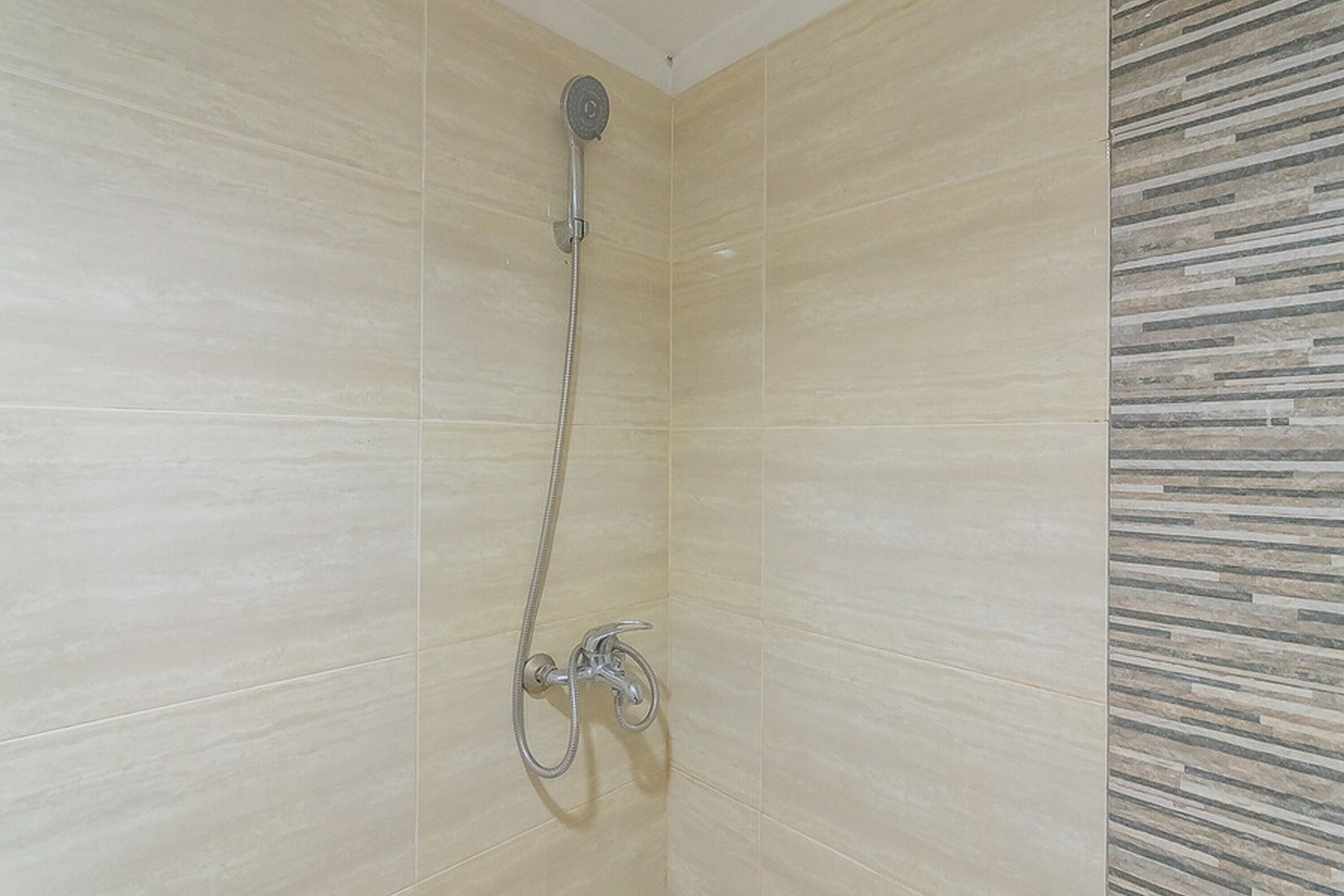 Eine Dusche mit Handbrause und Wandarmatur in einem gefliesten Raum.