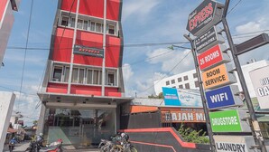 A hotel with a red and white facade, multiple rooms, and signs indicating room service, WiFi, and a drugstore. - RedDoorz near Stadion Sanaman Mantikei (Palangkaraya)
